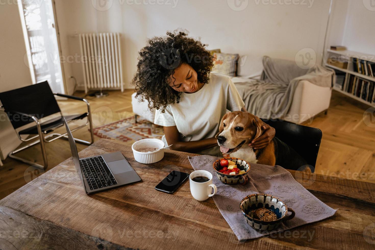 Black young woman strokes her dog while having breakfast at her home photo