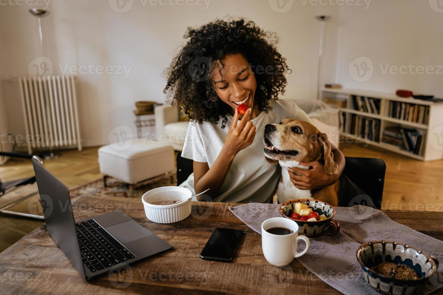 Black young woman playing with her dog while having breakfast photo