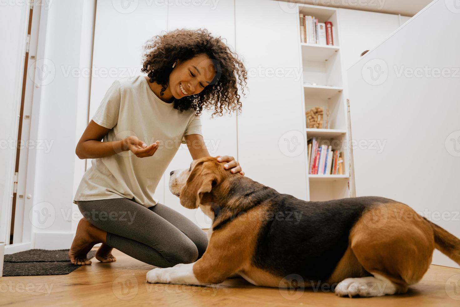 Joven negra en auriculares sonriendo mientras alimenta a su perro foto