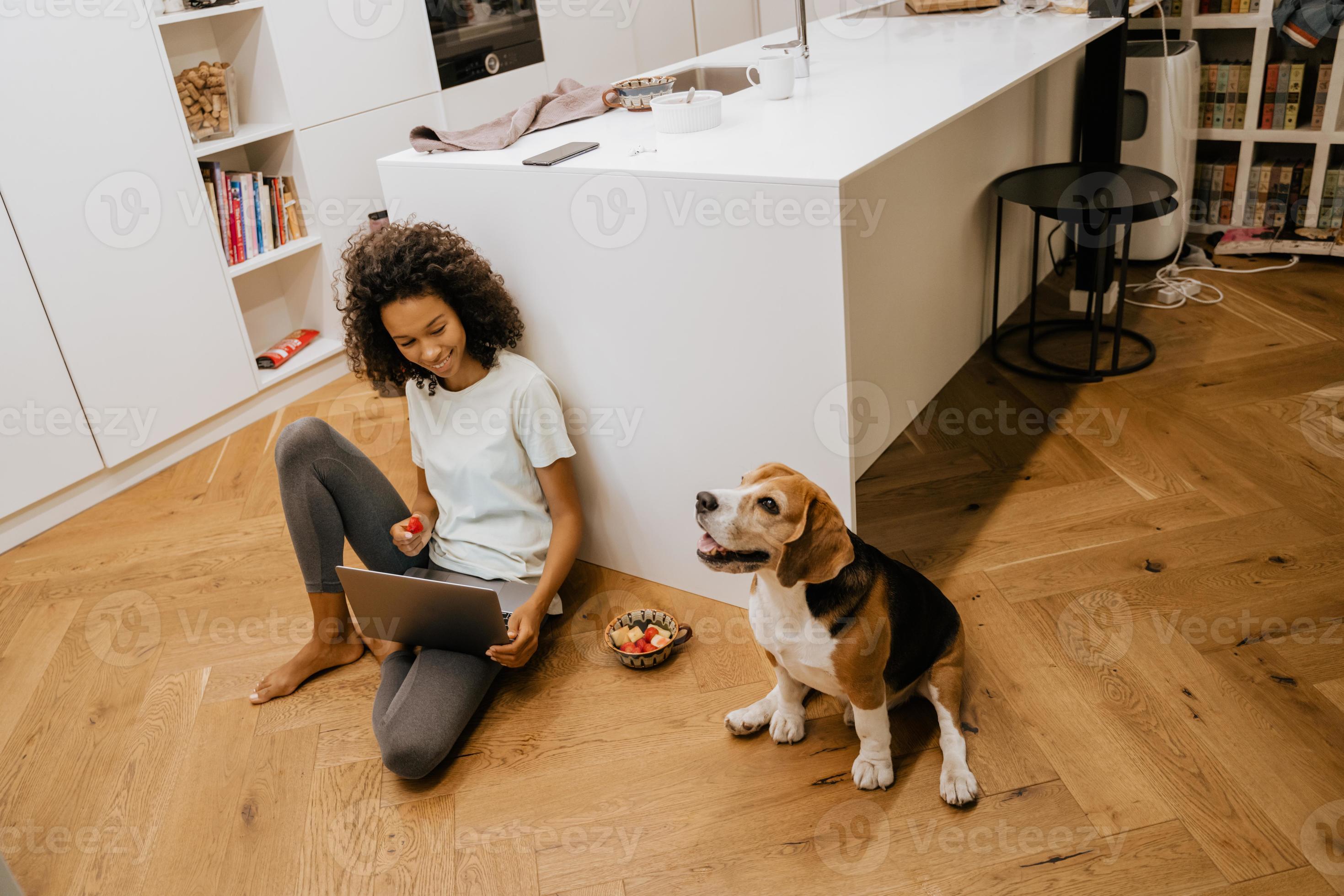 Black young woman using laptop and sitting with her dog in the kitchen photo