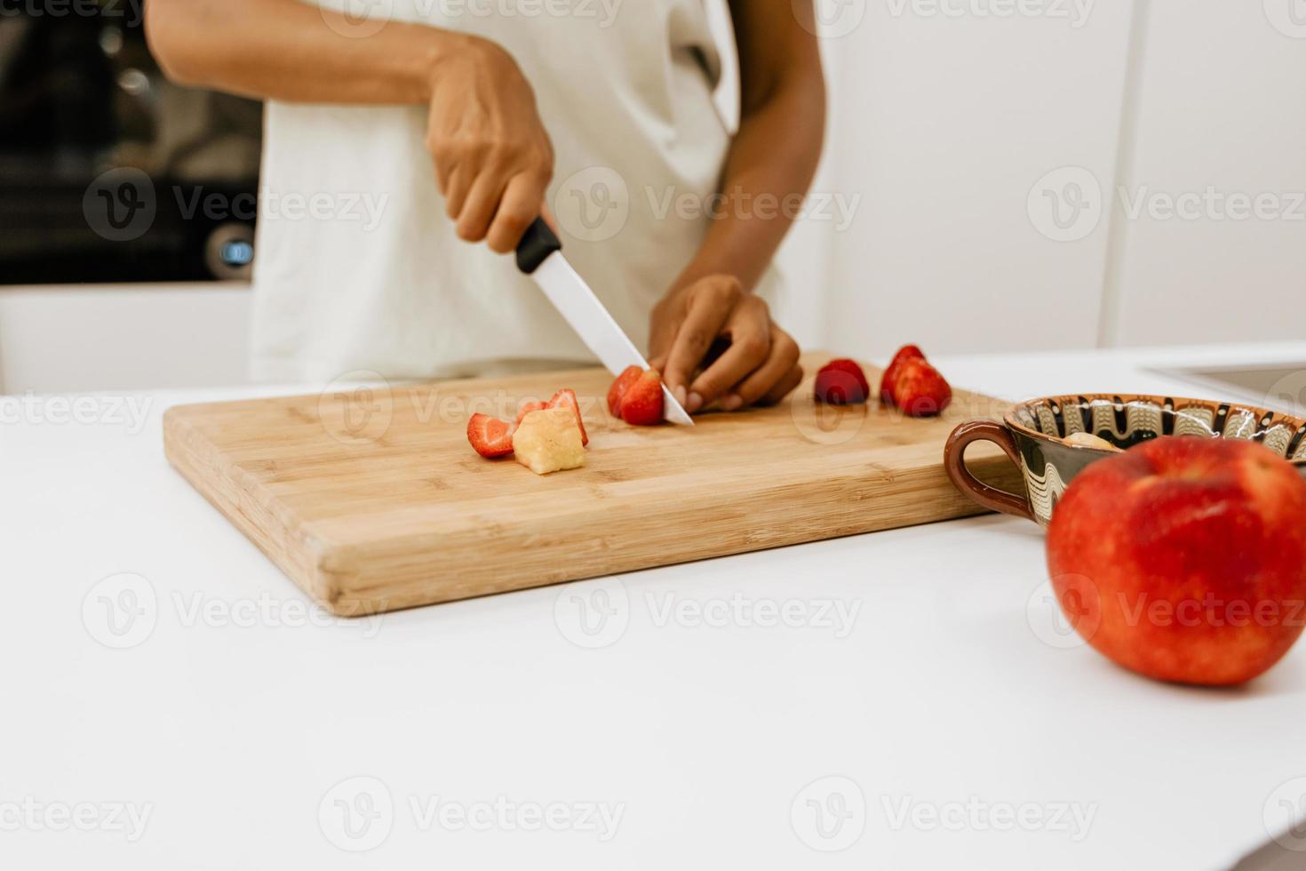 Black young woman cutting strawberries in the kitchen photo