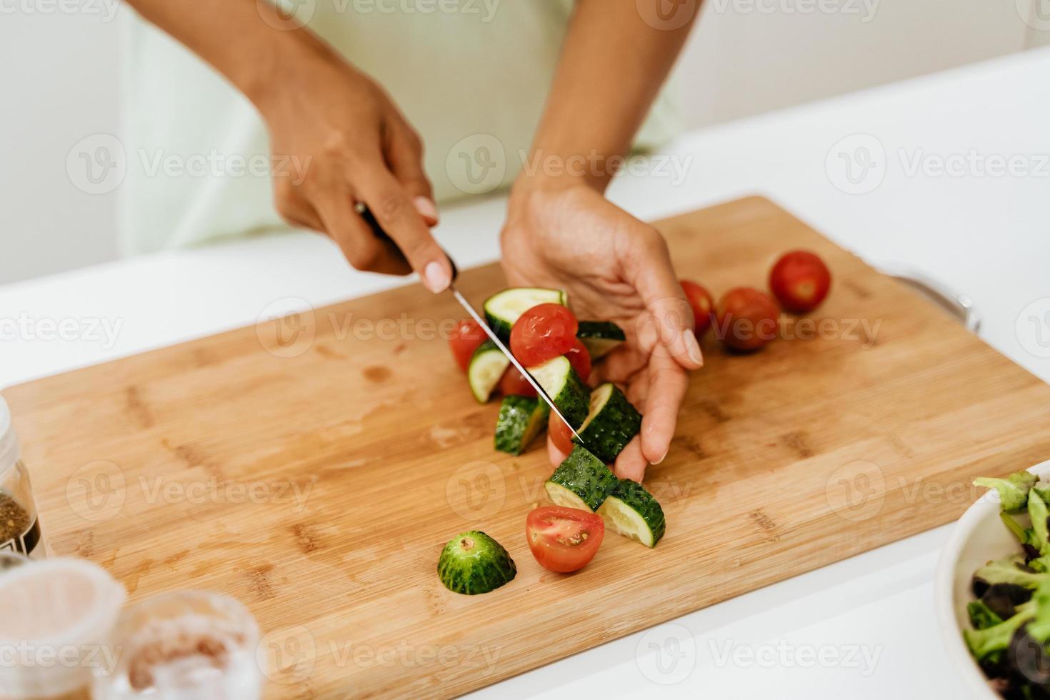 Joven negra haciendo ensalada mientras se cocina el almuerzo en la cocina foto