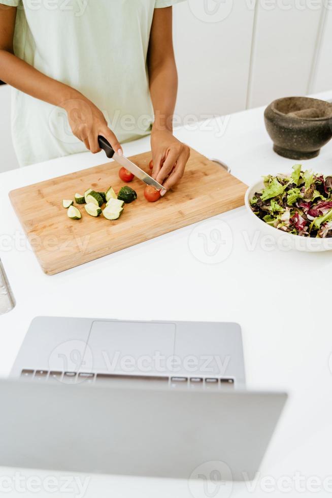 Joven negra haciendo ensalada mientras usa el portátil en la cocina foto