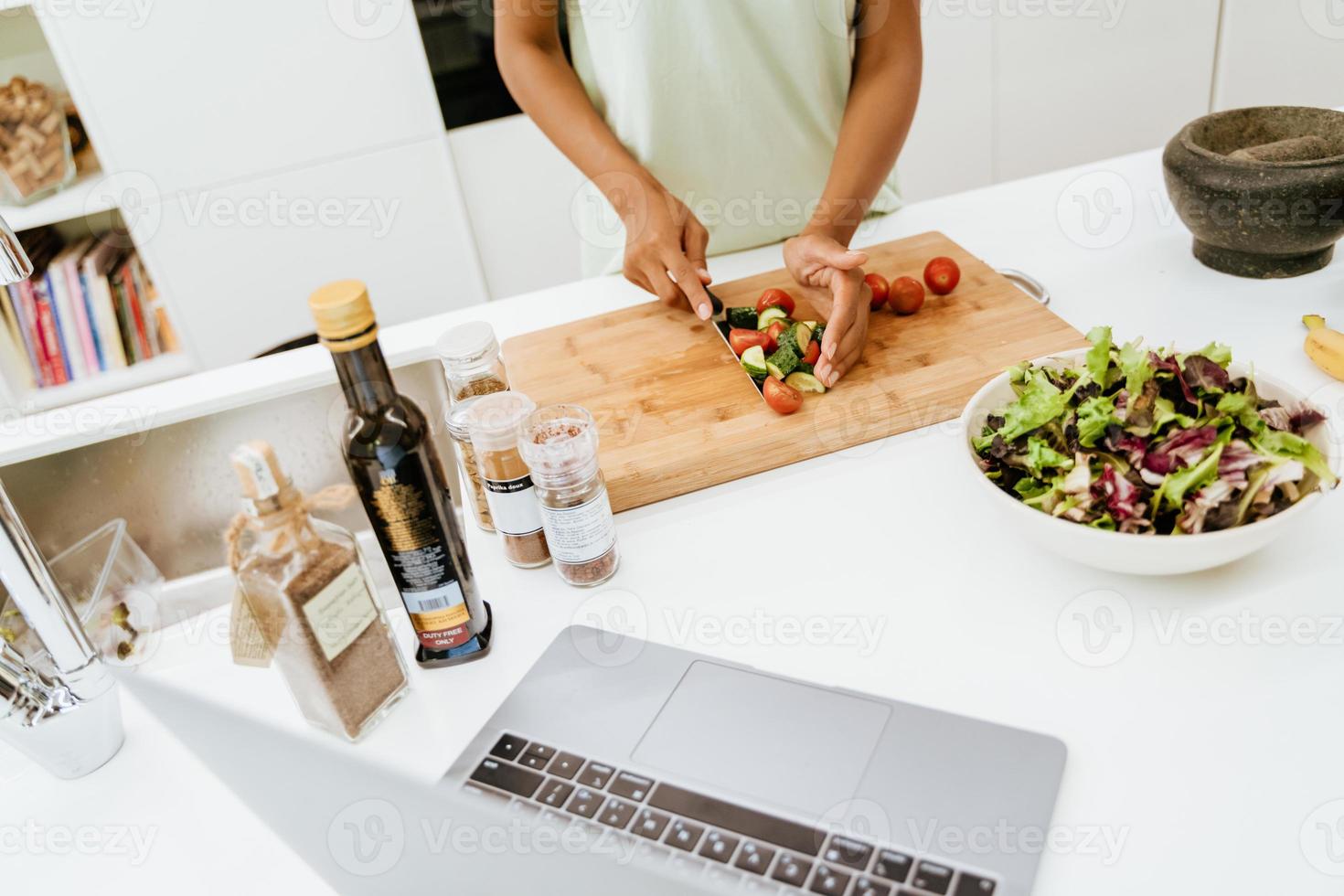 Joven negra haciendo ensalada mientras usa el portátil en la cocina foto