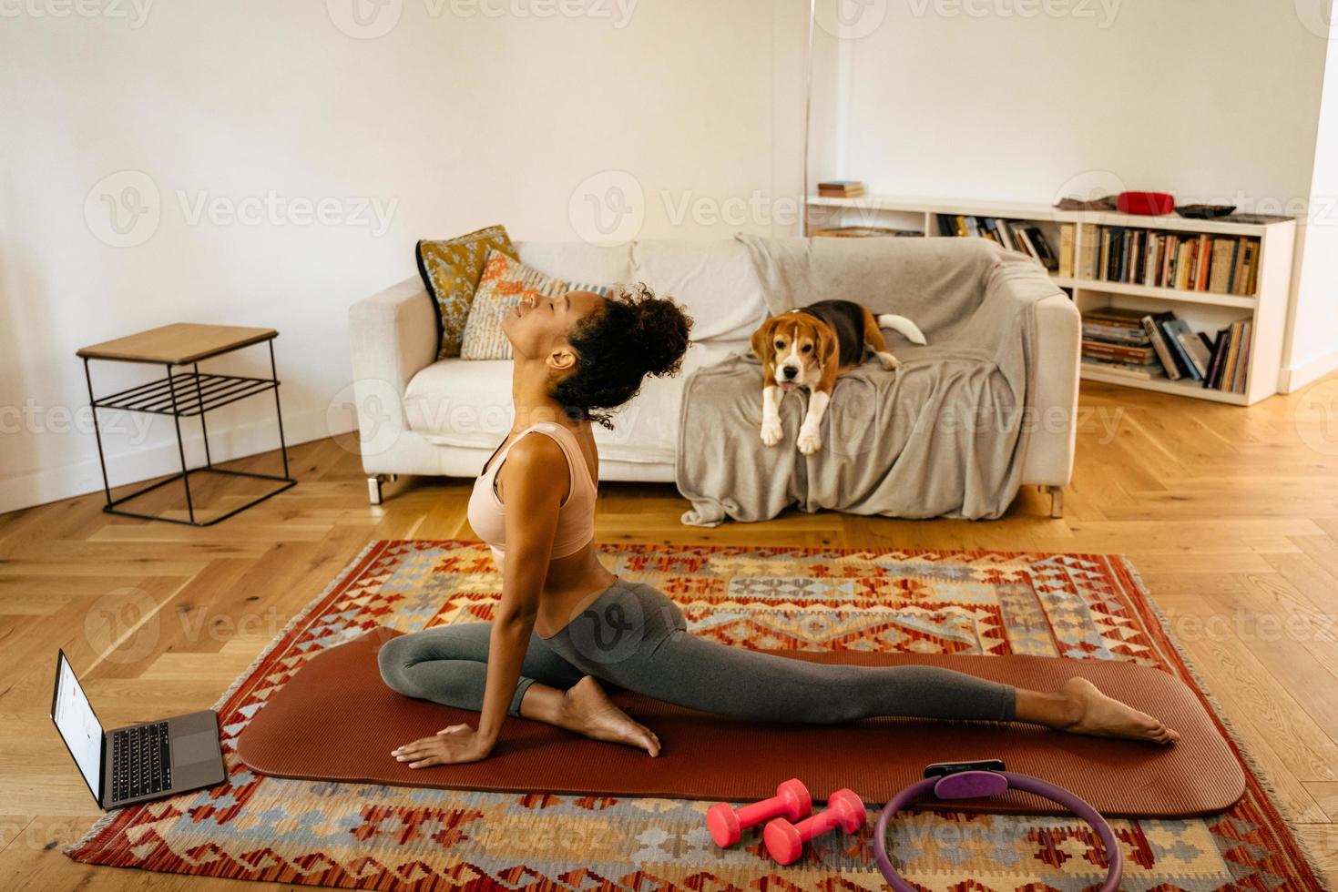 Black young woman stretching in yoga poses at home with her dog photo