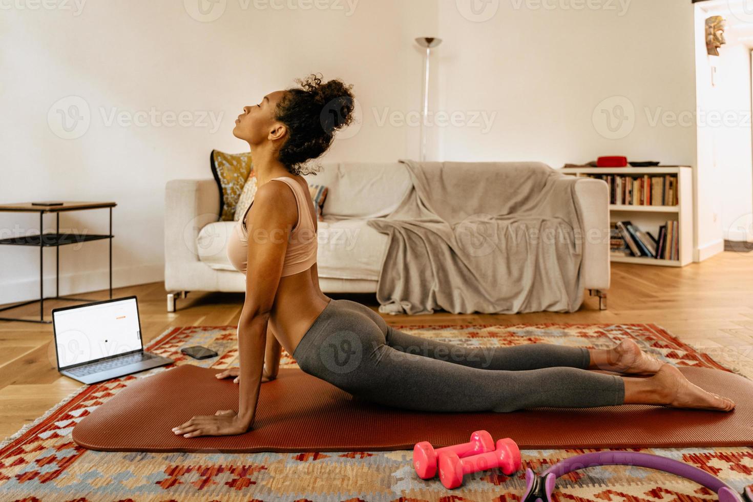 Black young woman doing yoga while using laptop at home photo