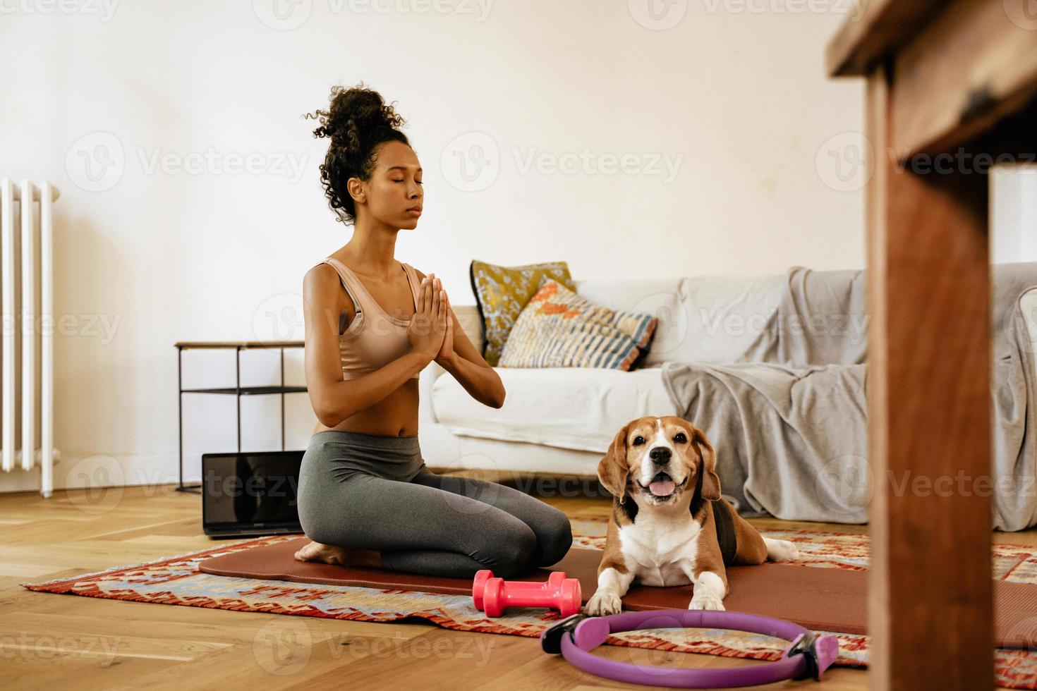 Joven negra meditando durante la práctica del yoga con su perro foto