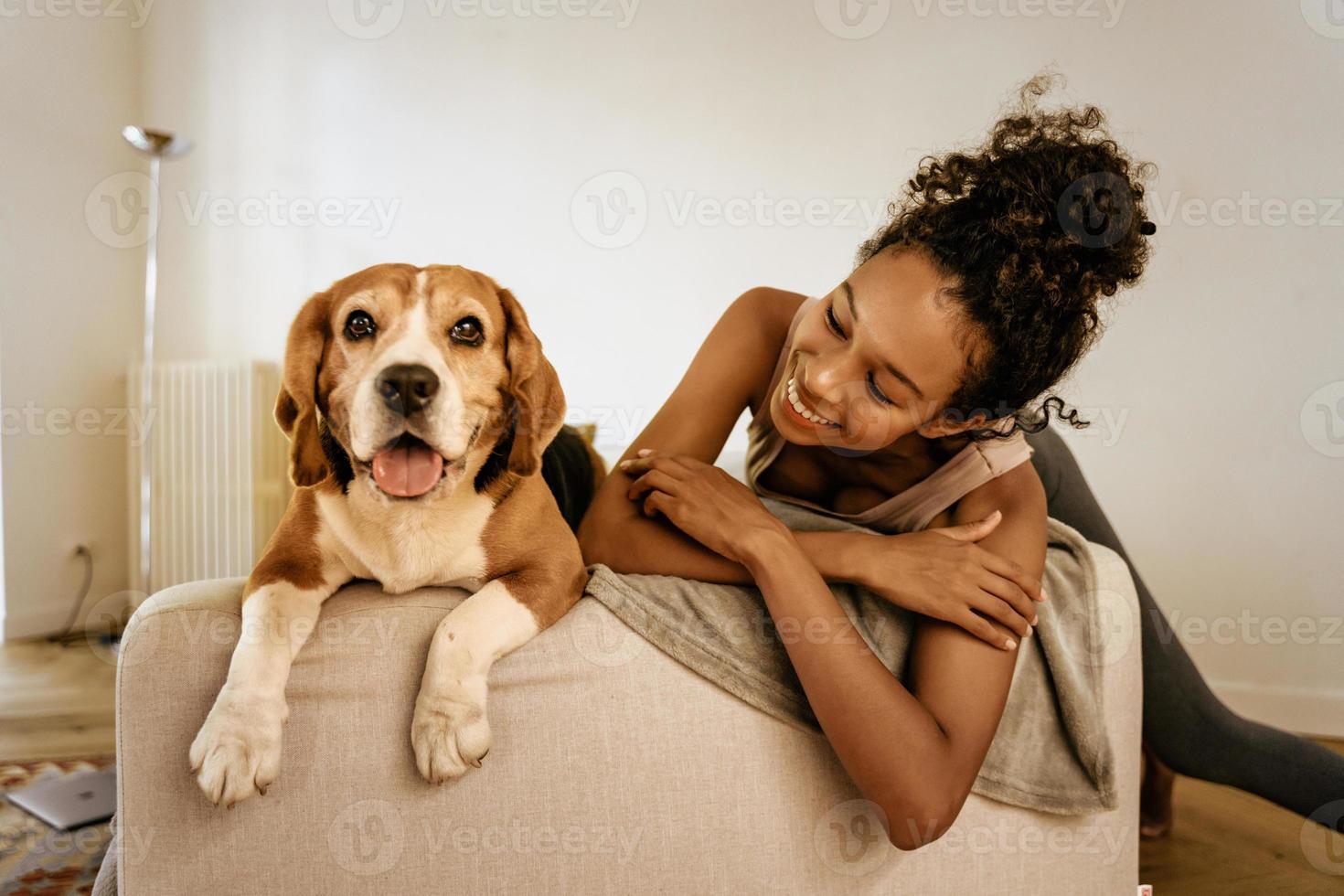 Joven negra riendo mientras descansa con su perro en el sofá foto