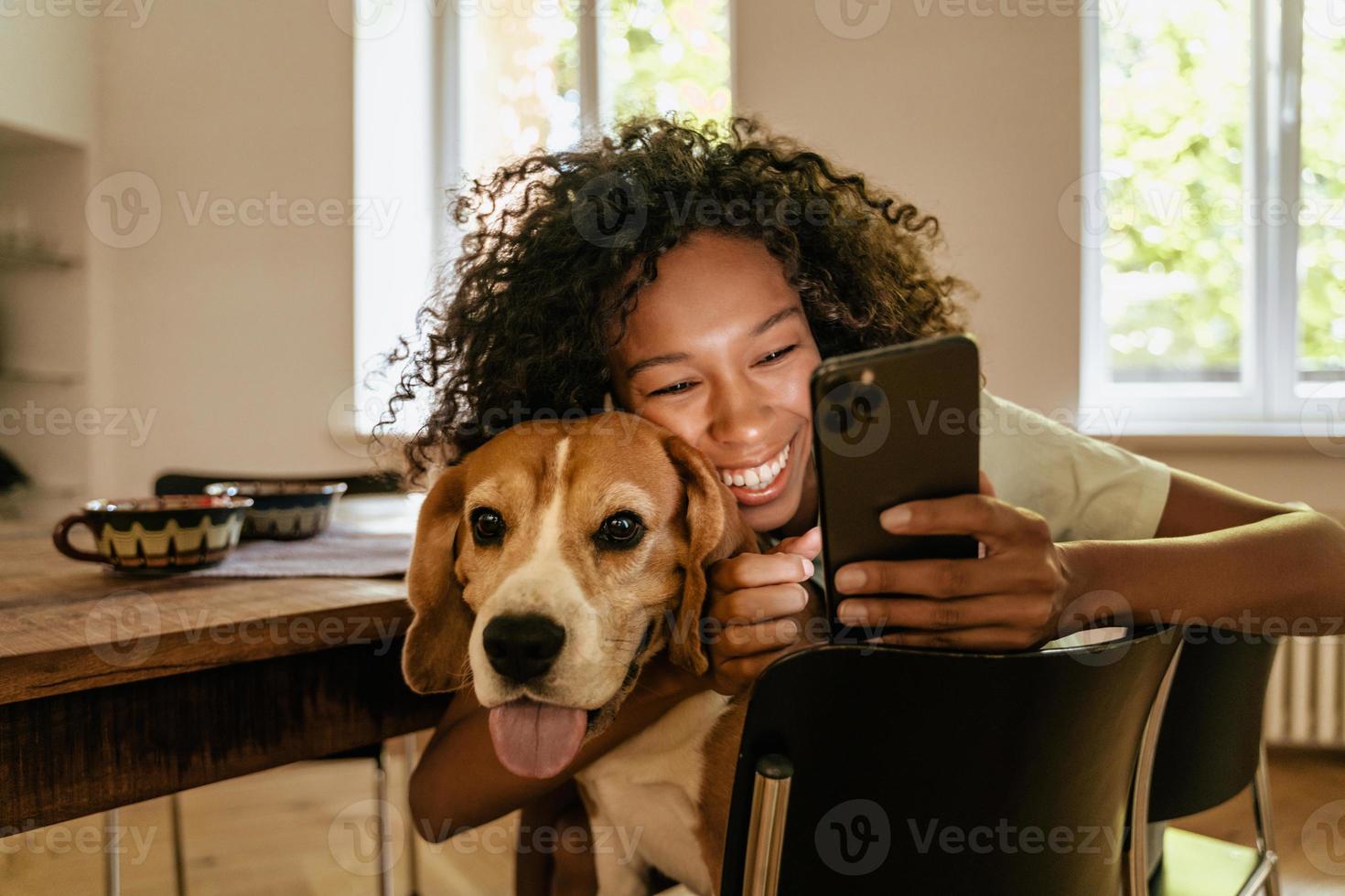 Joven negra abrazando con su perro mientras usa el teléfono móvil foto