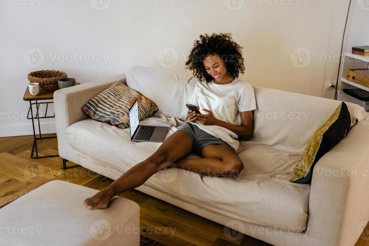 Black young woman resting on sofa while using cellphone  photo