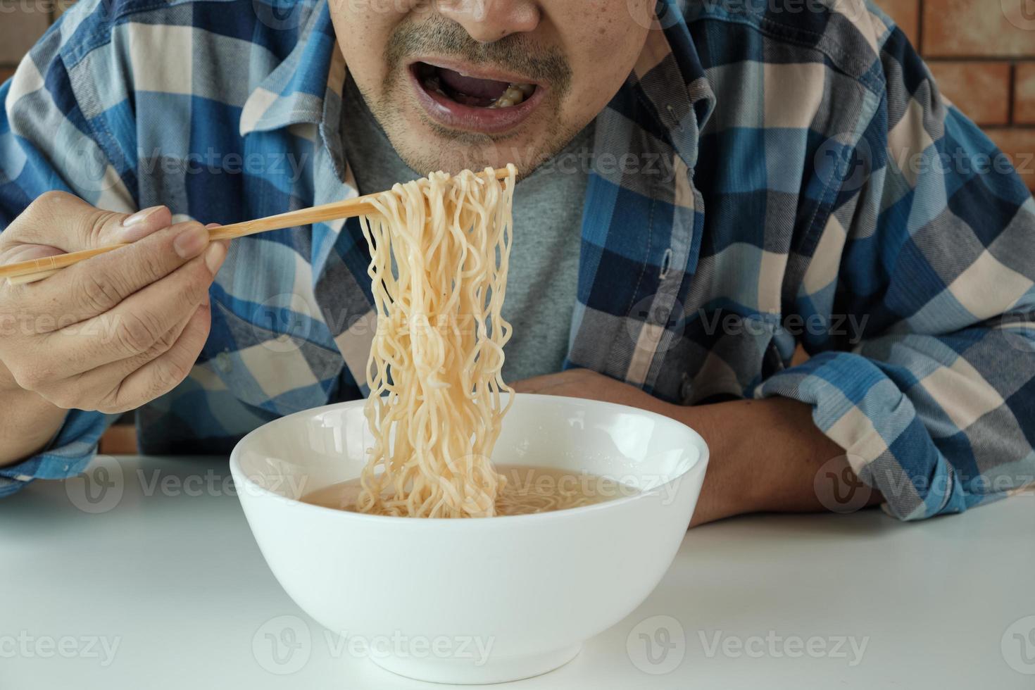 El hombre tailandés casual hambriento usa palillos para comer fideos instantáneos calientes en una taza blanca durante el almuerzo, rápido, sabroso y barato. comida tradicional asiática sana de comida rápida de estilo de vida japonés y chino. foto