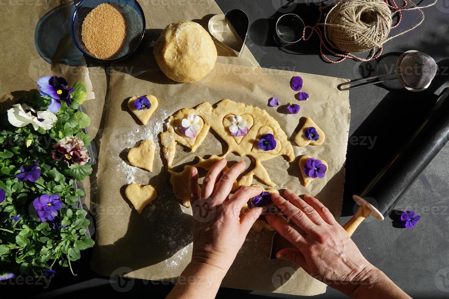 manos de mujer haciendo galletas en forma de corazón con flor heartsease. foto