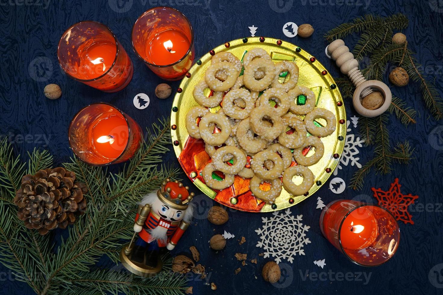 rama de pino verde, pasteles navideños tradicionales en la placa de oro y velas rojas sobre la mesa. hermoso fondo festivo azul oscuro. foto