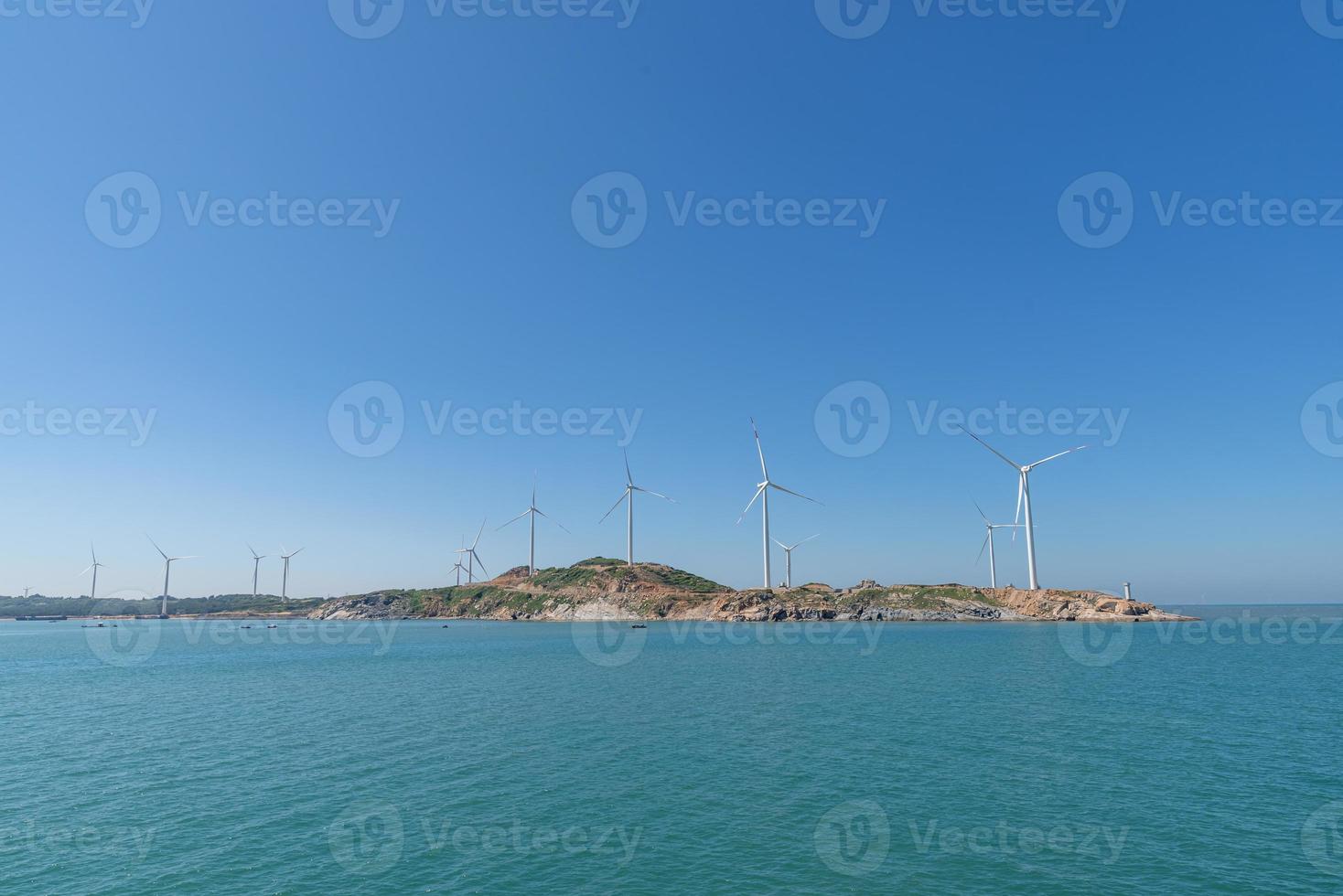 On the island in the middle of the sea, many wind turbines are installed under the blue sky photo