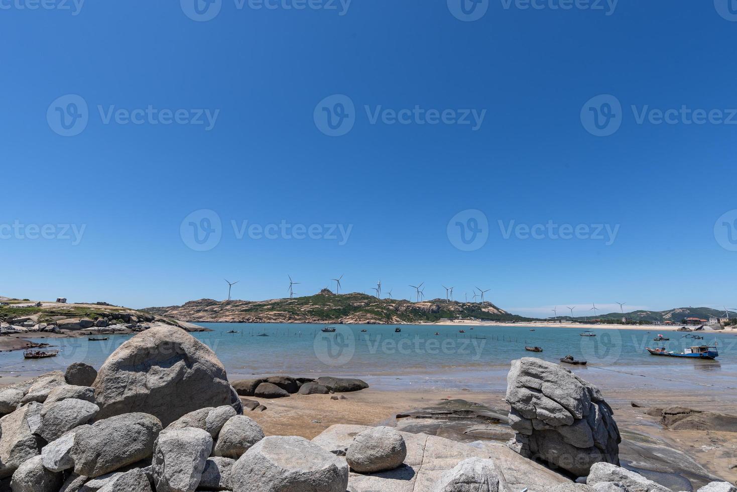 Stand high and watch the sea scenery under the blue sky, blue water, white waves and black rocks photo