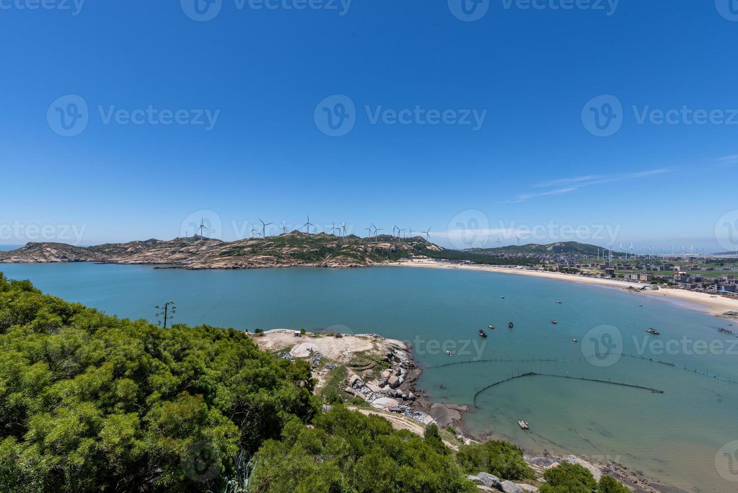 Stand high and watch the sea scenery under the blue sky, blue water, white waves and black rocks photo