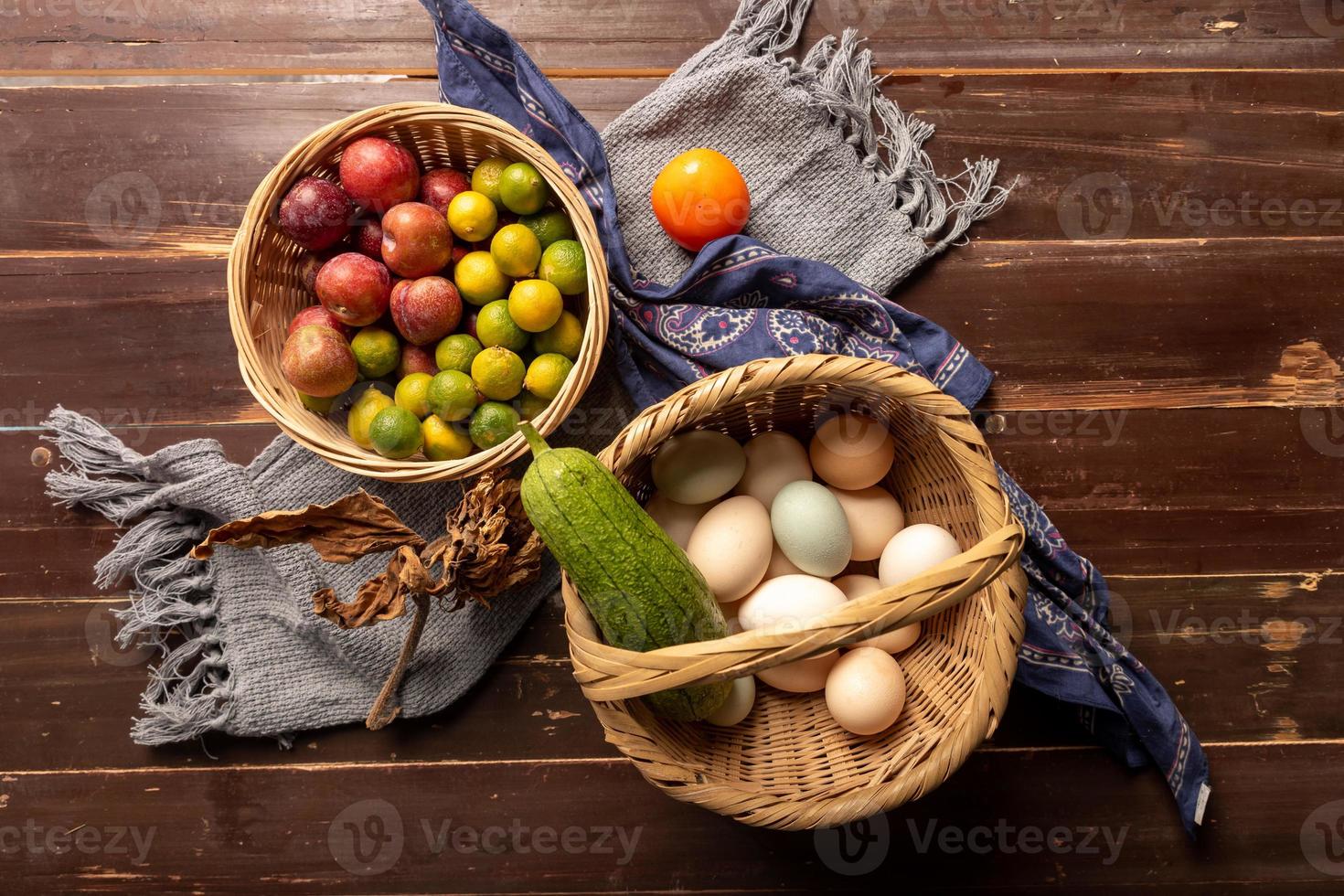 The eggs and other fruits and vegetables in the basket are on the wood grain table photo