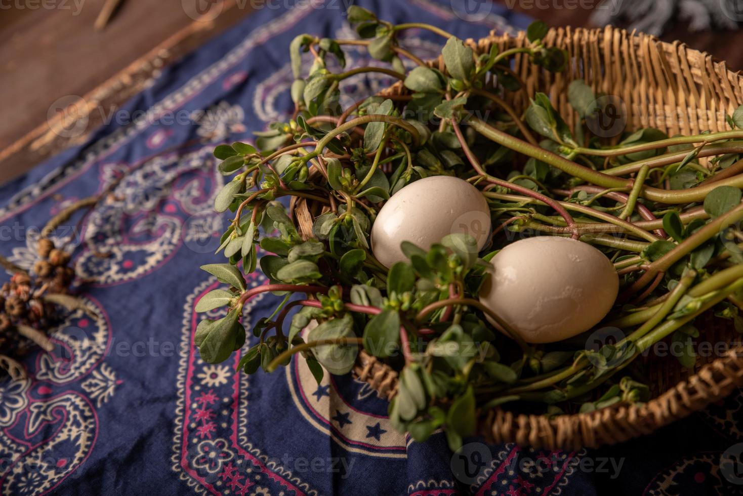 Los huevos y otras frutas y verduras de la canasta están en la mesa de madera. foto