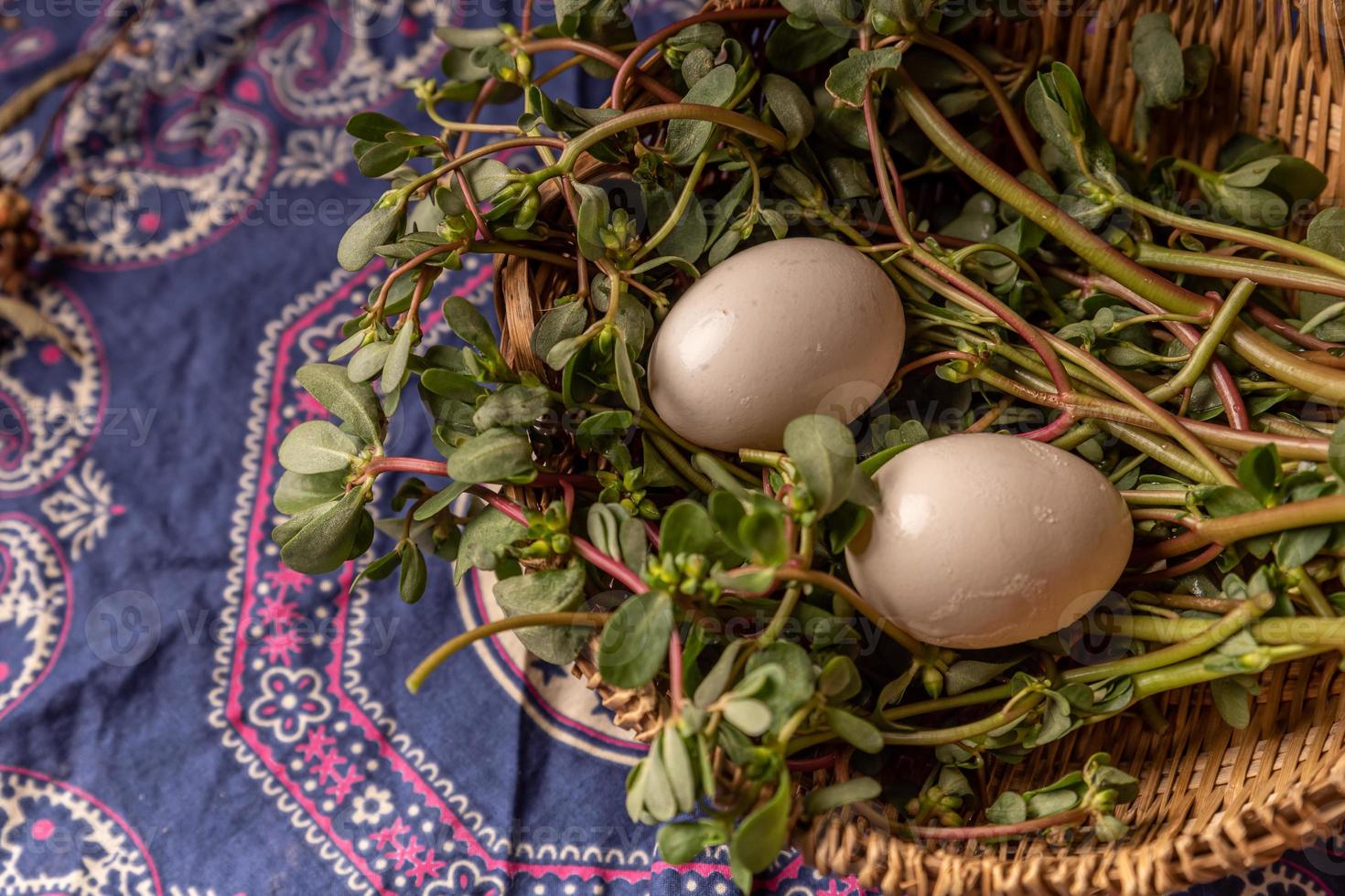 Los huevos y otras frutas y verduras de la canasta están en la mesa de madera. foto