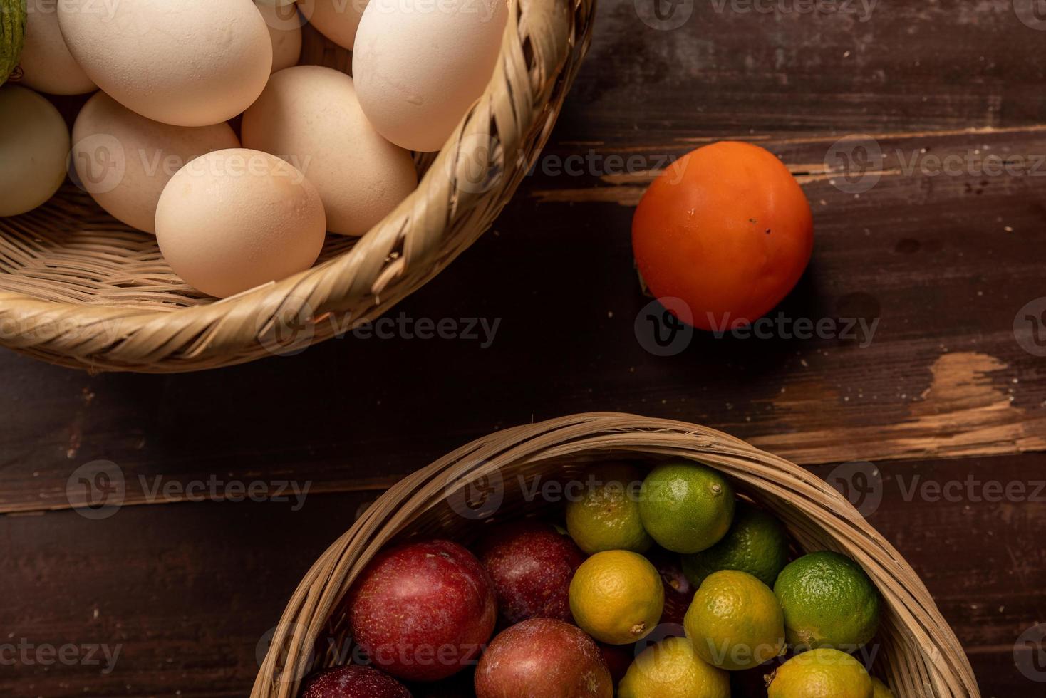 The eggs and other fruits and vegetables in the basket are on the wood grain table photo