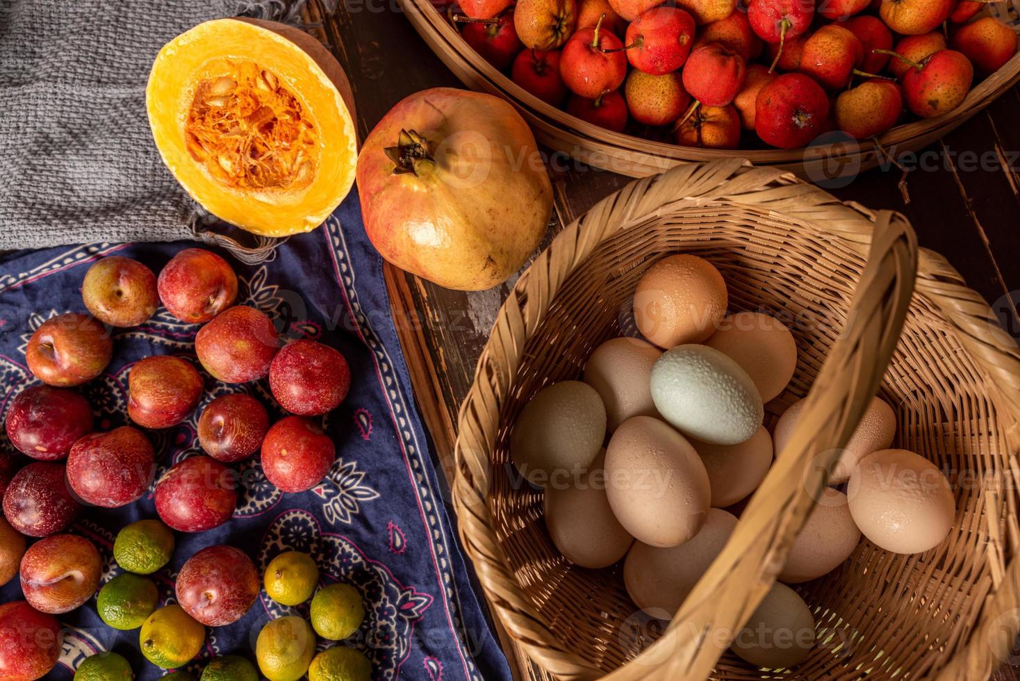 The eggs and other fruits and vegetables in the basket are on the wood grain table photo