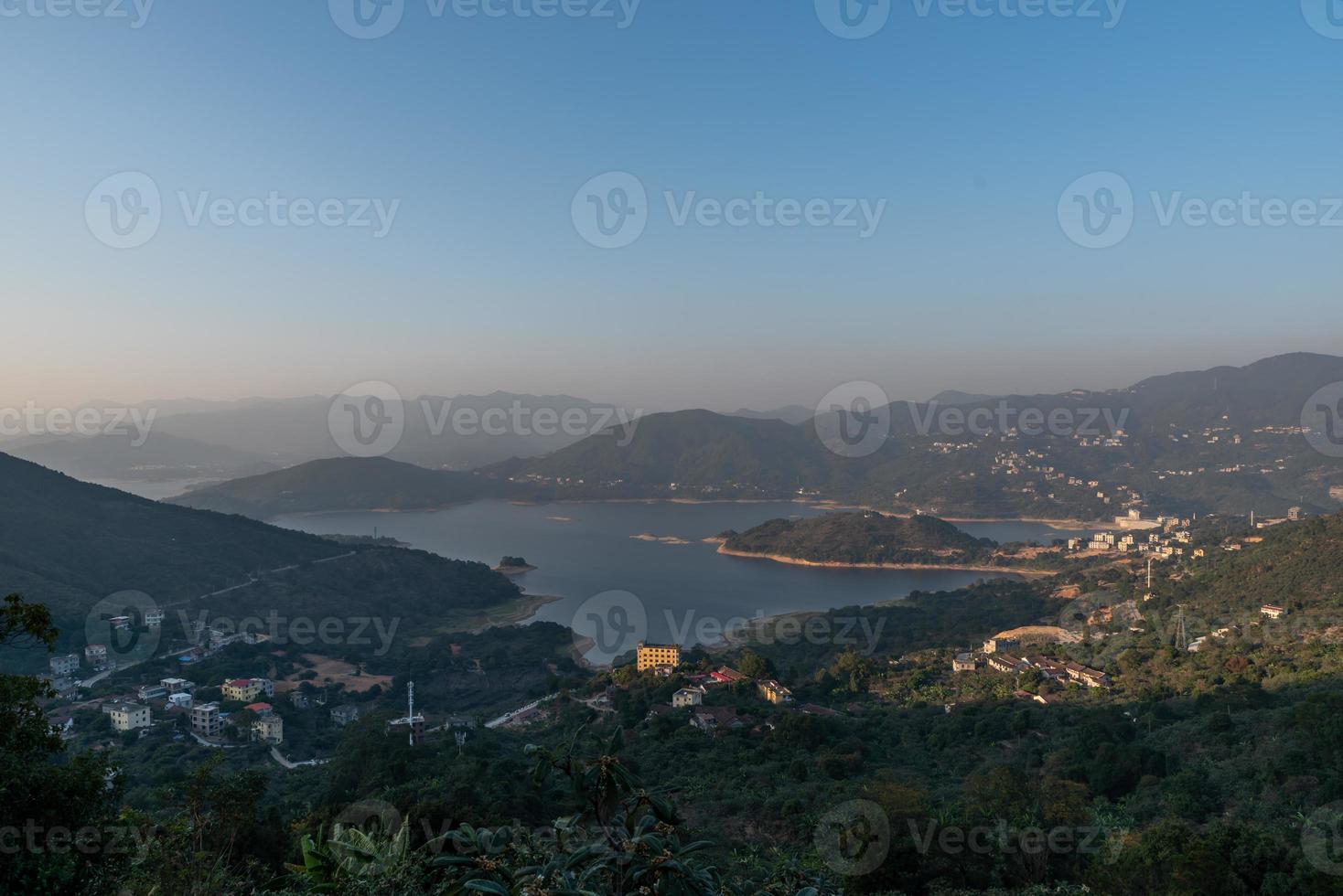 el embalse bajo el cielo azul y las nubes blancas está rodeado de montañas y bosques foto