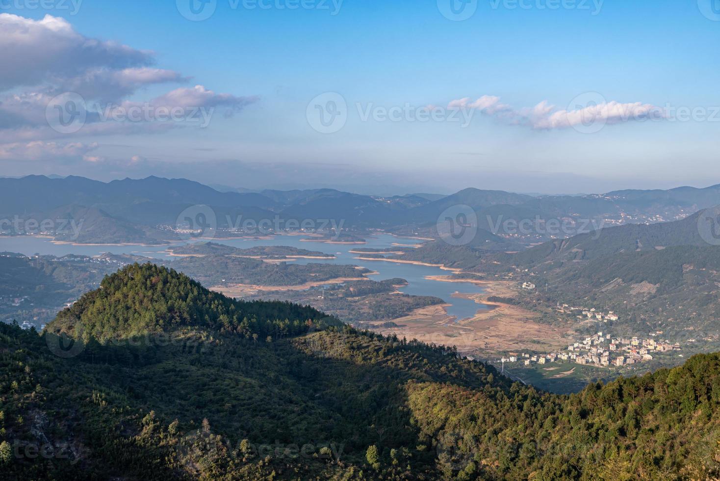 The reservoir under the blue sky and white clouds is surrounded by mountains and forests photo