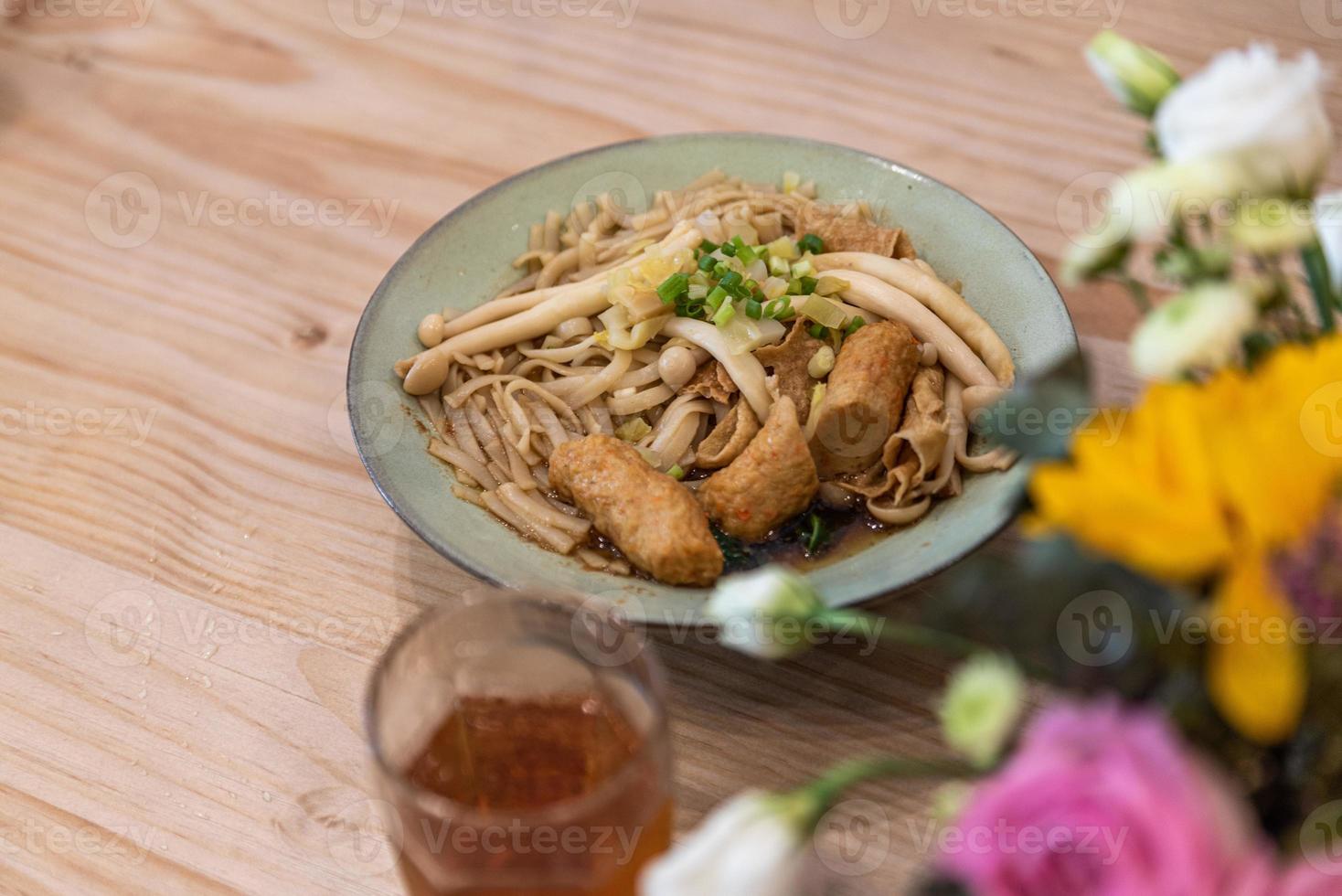 A bowl of noodle soup with sausage, vegetables and meat is on the table photo