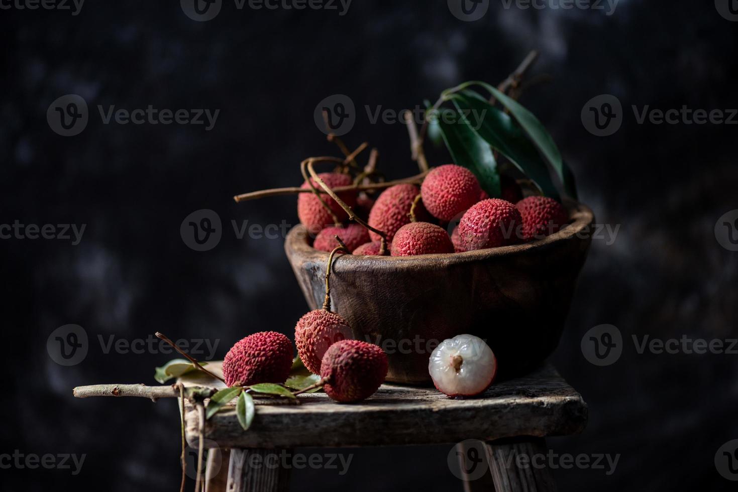 Litchi is placed in a wooden plate, peeled or unopened, on a dark wood grain table photo