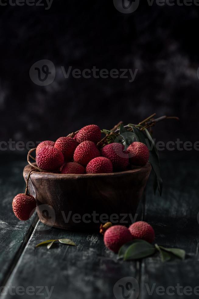 El litchi se coloca en un plato de madera, pelado o sin abrir, sobre una mesa de madera oscura. foto