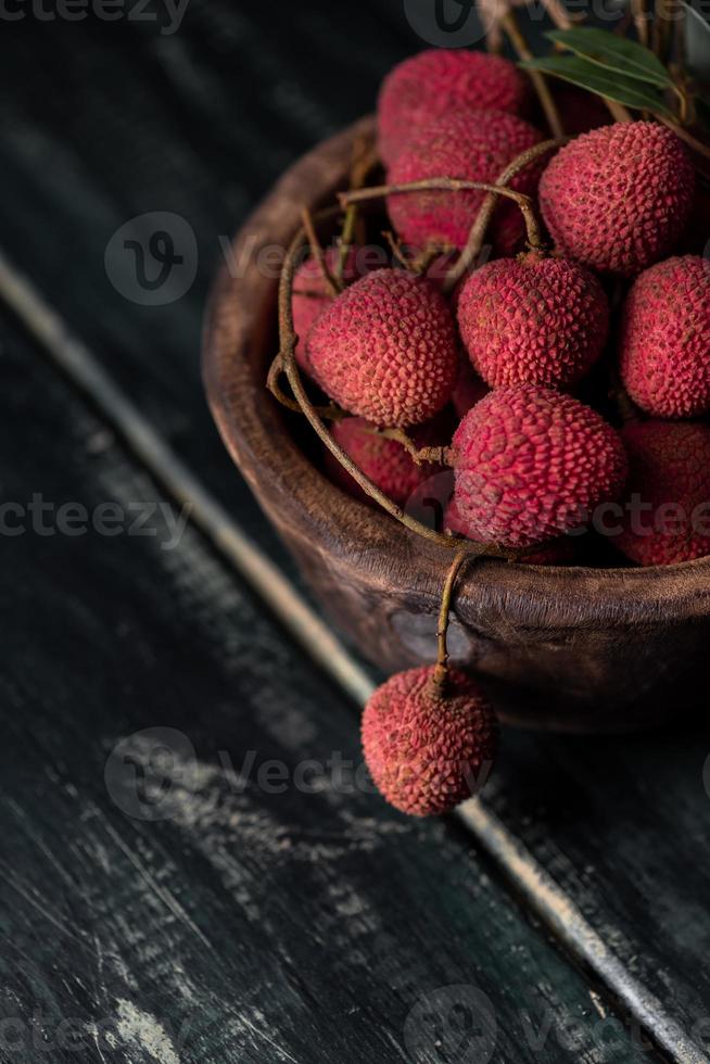 Litchi is placed in a wooden plate, peeled or unopened, on a dark wood grain table photo