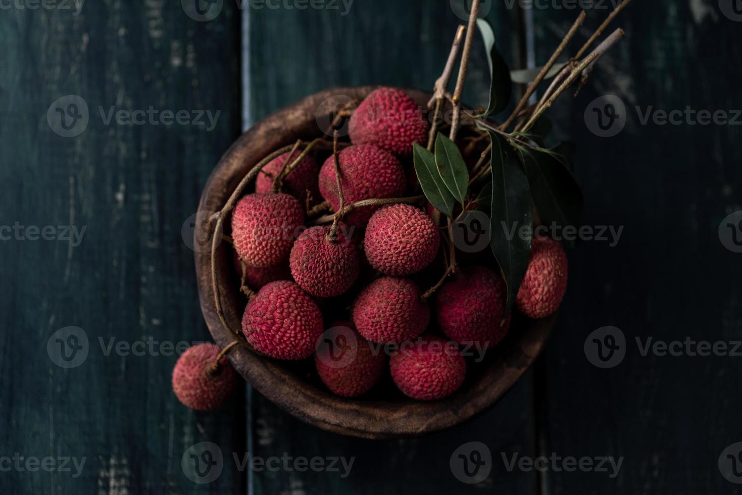 El litchi se coloca en un plato de madera, pelado o sin abrir, sobre una mesa de madera oscura. foto