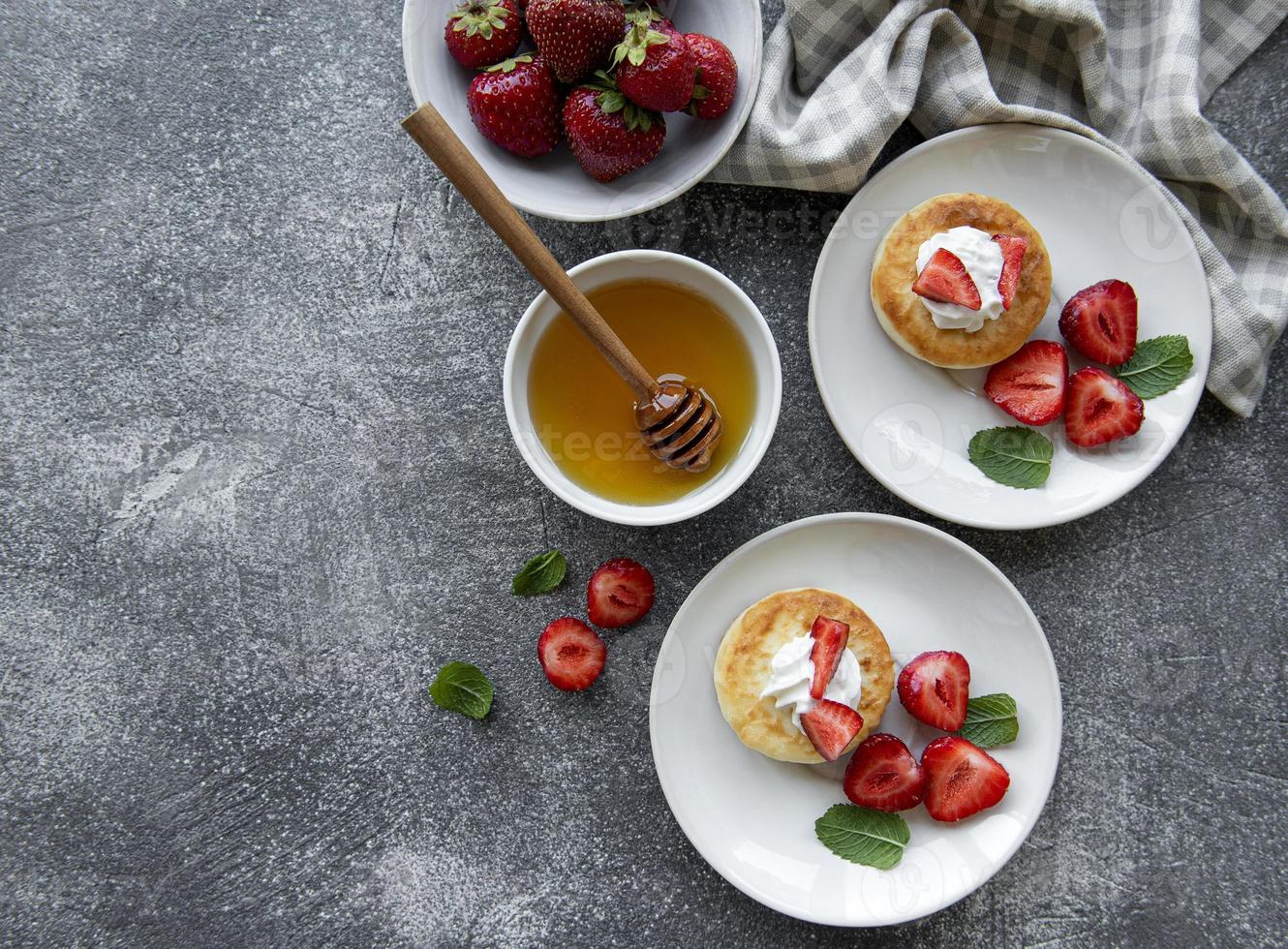 Tortitas de requesón, buñuelos de ricotta en placa de cerámica con fresa fresca foto