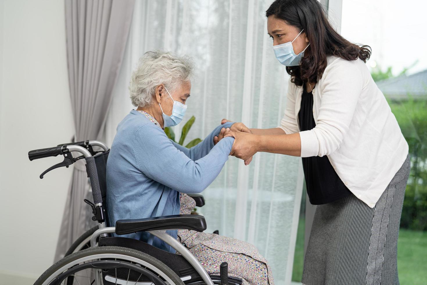 Ayude a una anciana asiática mayor o anciana sentada en una silla de ruedas y con una mascarilla para proteger la seguridad de la infección por el coronavirus covid-19 foto