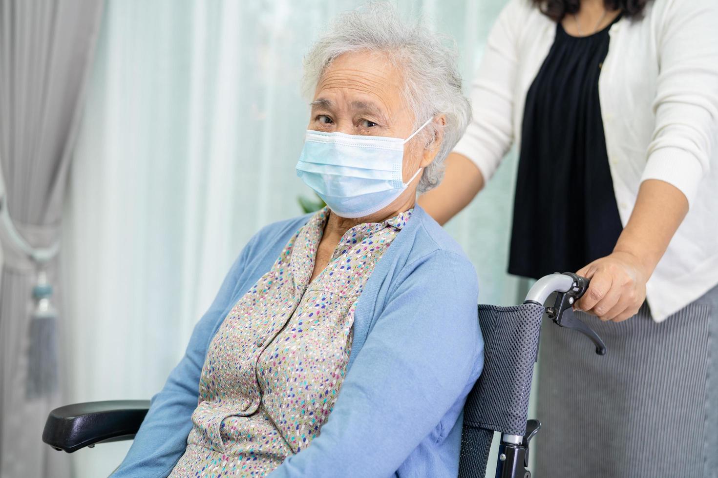 Ayude a una anciana asiática mayor o anciana sentada en una silla de ruedas y con una mascarilla para proteger la seguridad de la infección por el coronavirus covid-19 foto