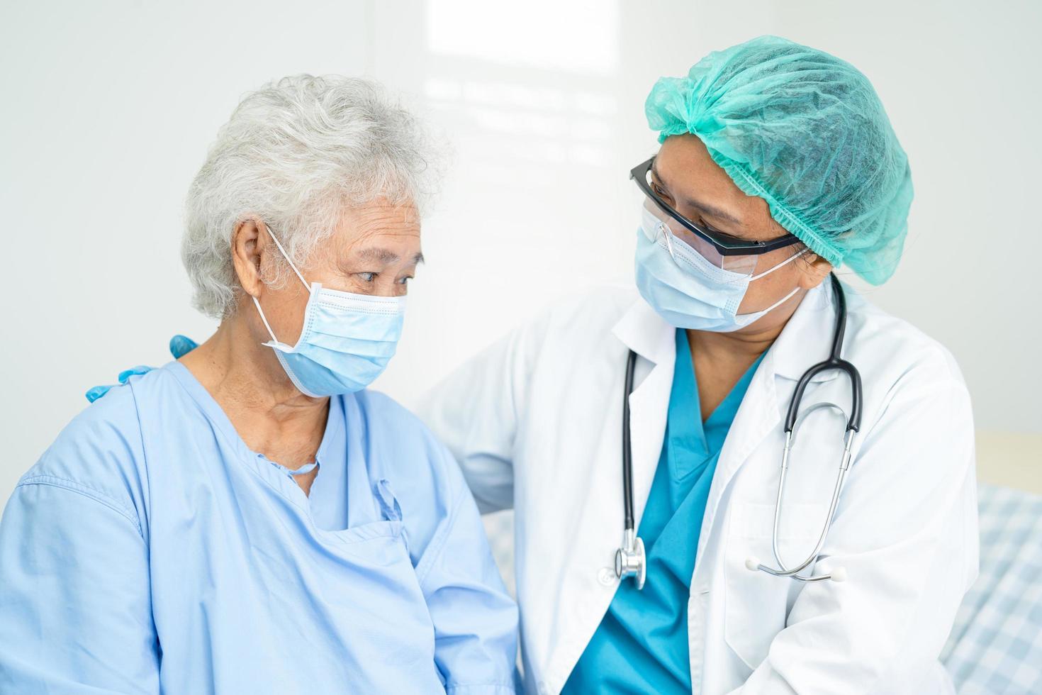 Doctor help Asian senior or elderly old lady woman patient wearing a face mask in hospital for protect safety infection and kill Covid-19 Coronavirus photo