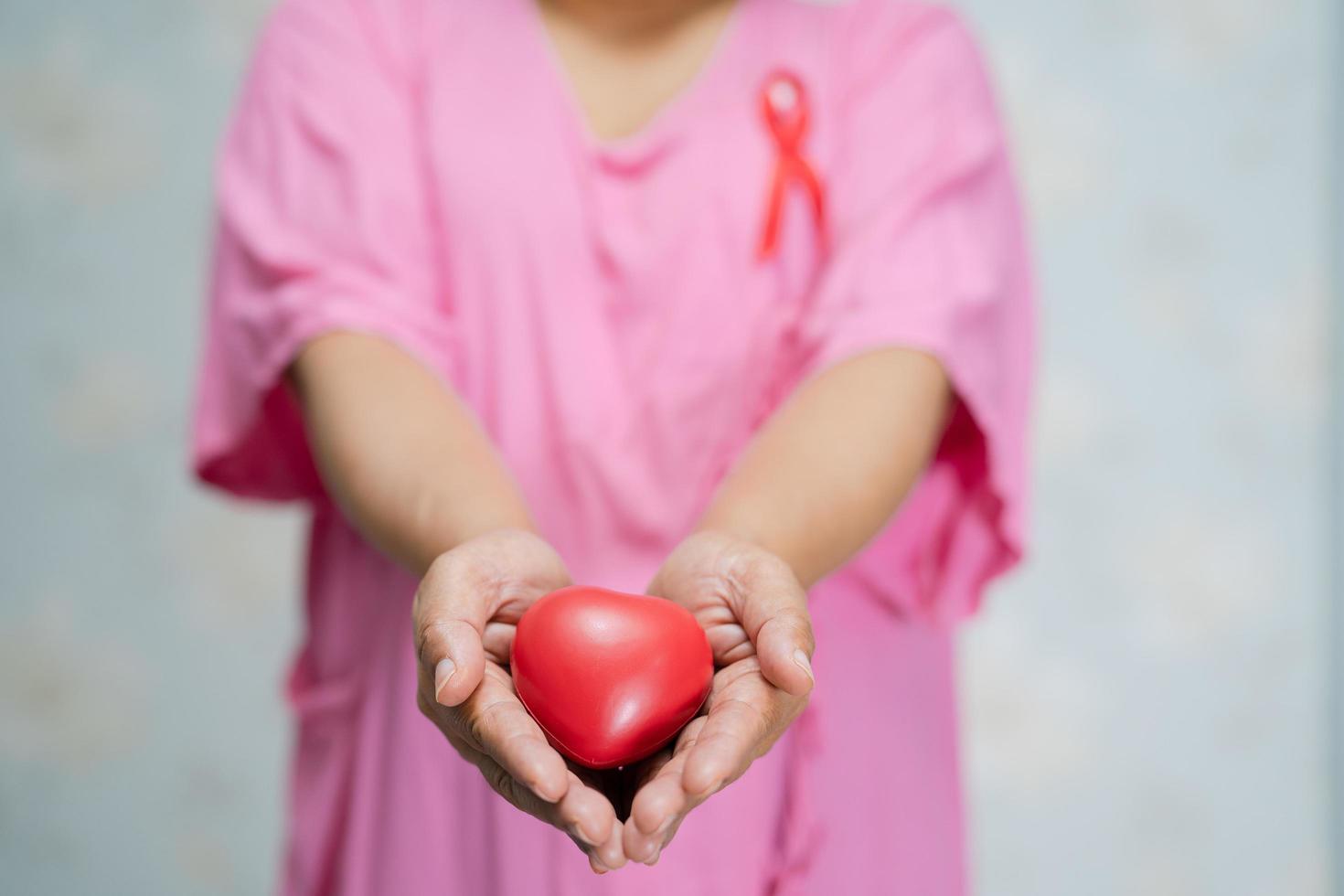 Asian lady woman patient holding red heart in hand at hospital, symbol of World Breast Cancer Day photo