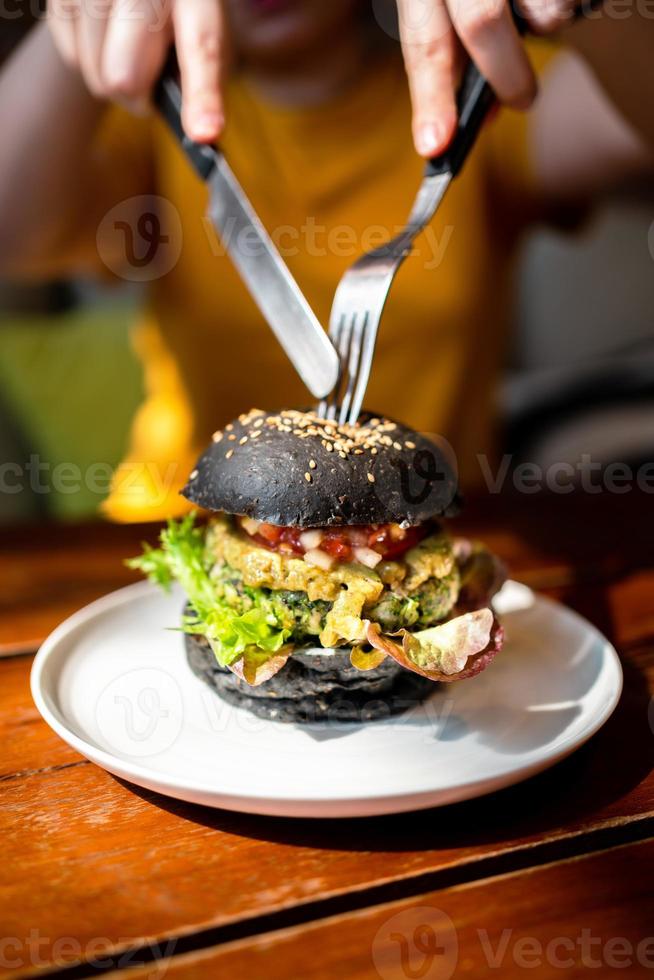 Hands cut Broccoli quinoa charcoal burger with guacamole by knife. photo