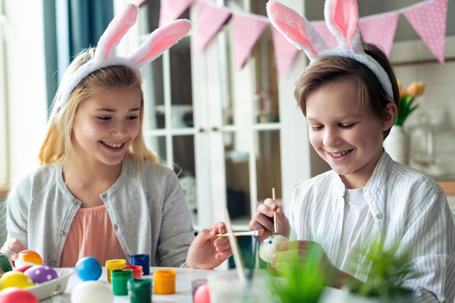 Two joyful children paint easter eggs in rabbit ears. photo