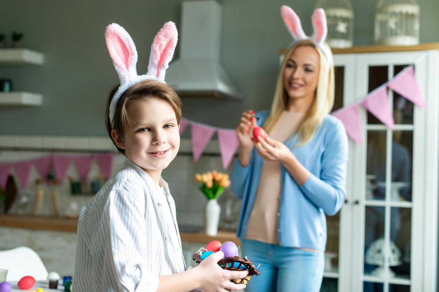 Cute boy holding a basket with colored eggs. On a blurred background, his mother paints an Easter egg. photo