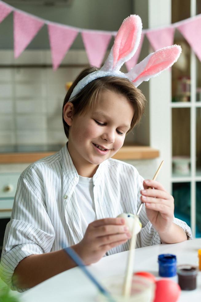 Smiling boy close up in easter bunny coloring easter egg. photo