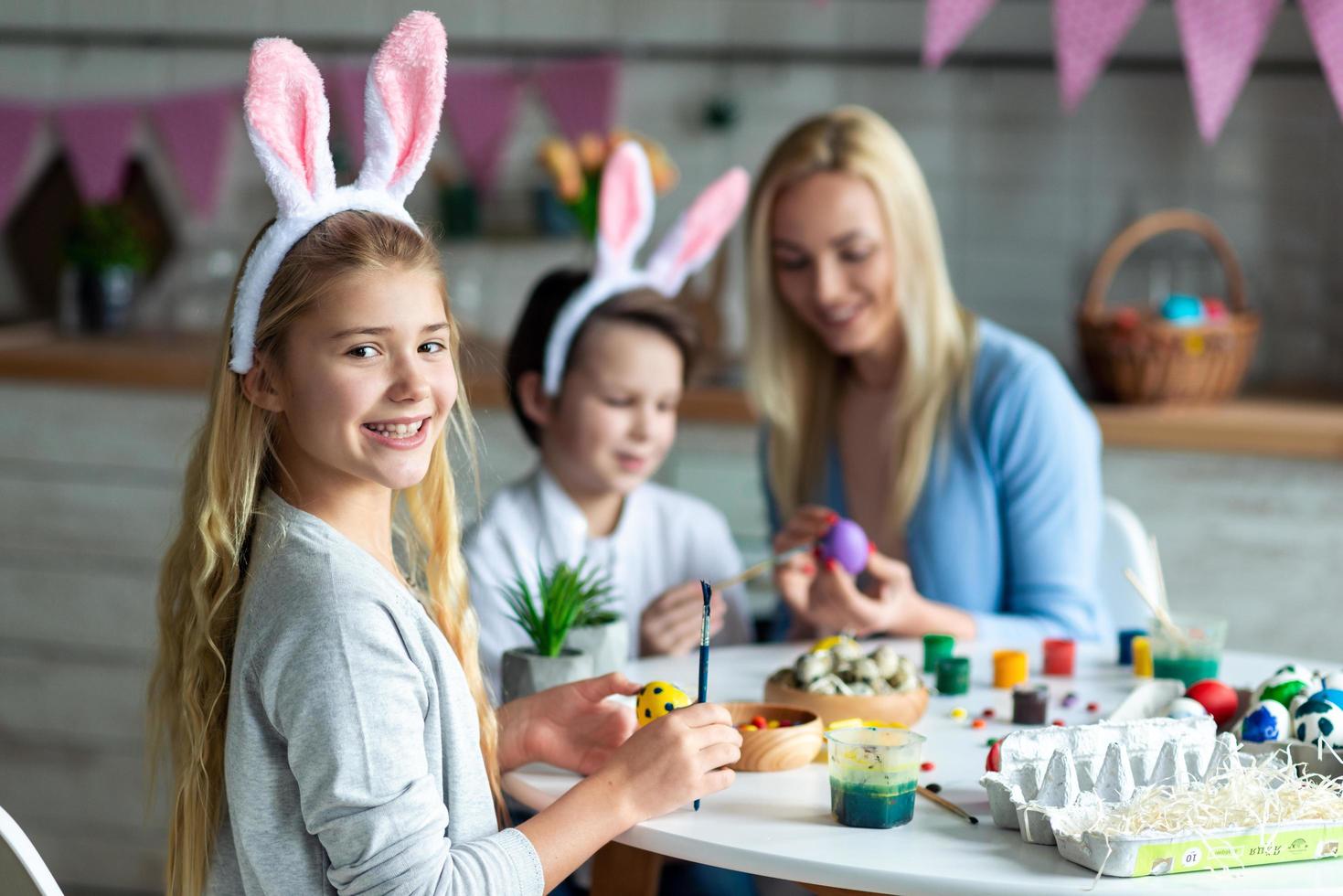 de cerca, niña sonriente mirando a cámara, pintando huevos de Pascua. foto