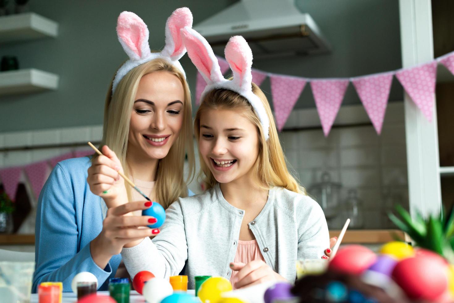 Mom and her daughter are painting an Easter egg in the kitchen. Happy Easter concept. photo