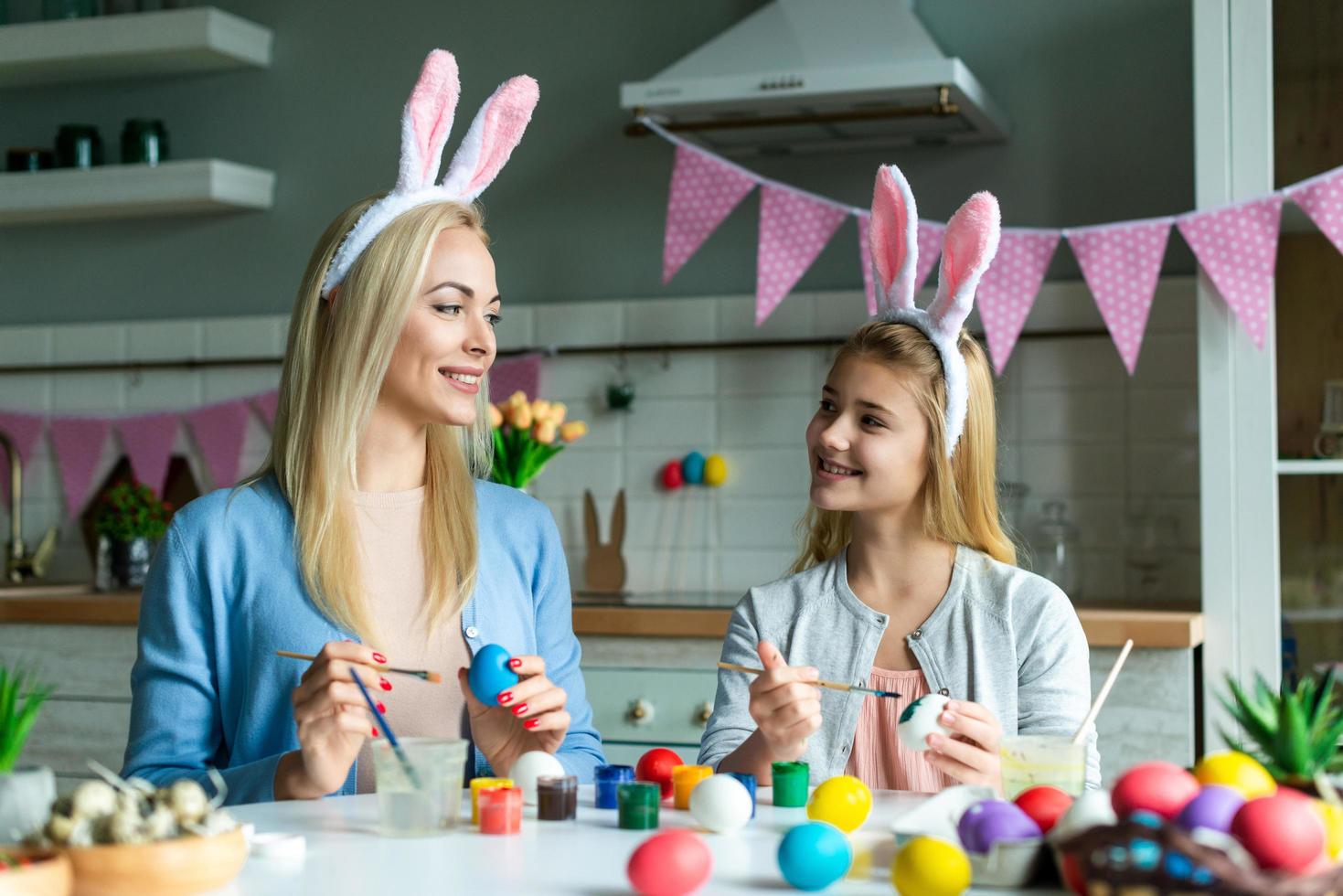 Mom with daughter in bunny ears paint Easter eggs in the kitchen. photo