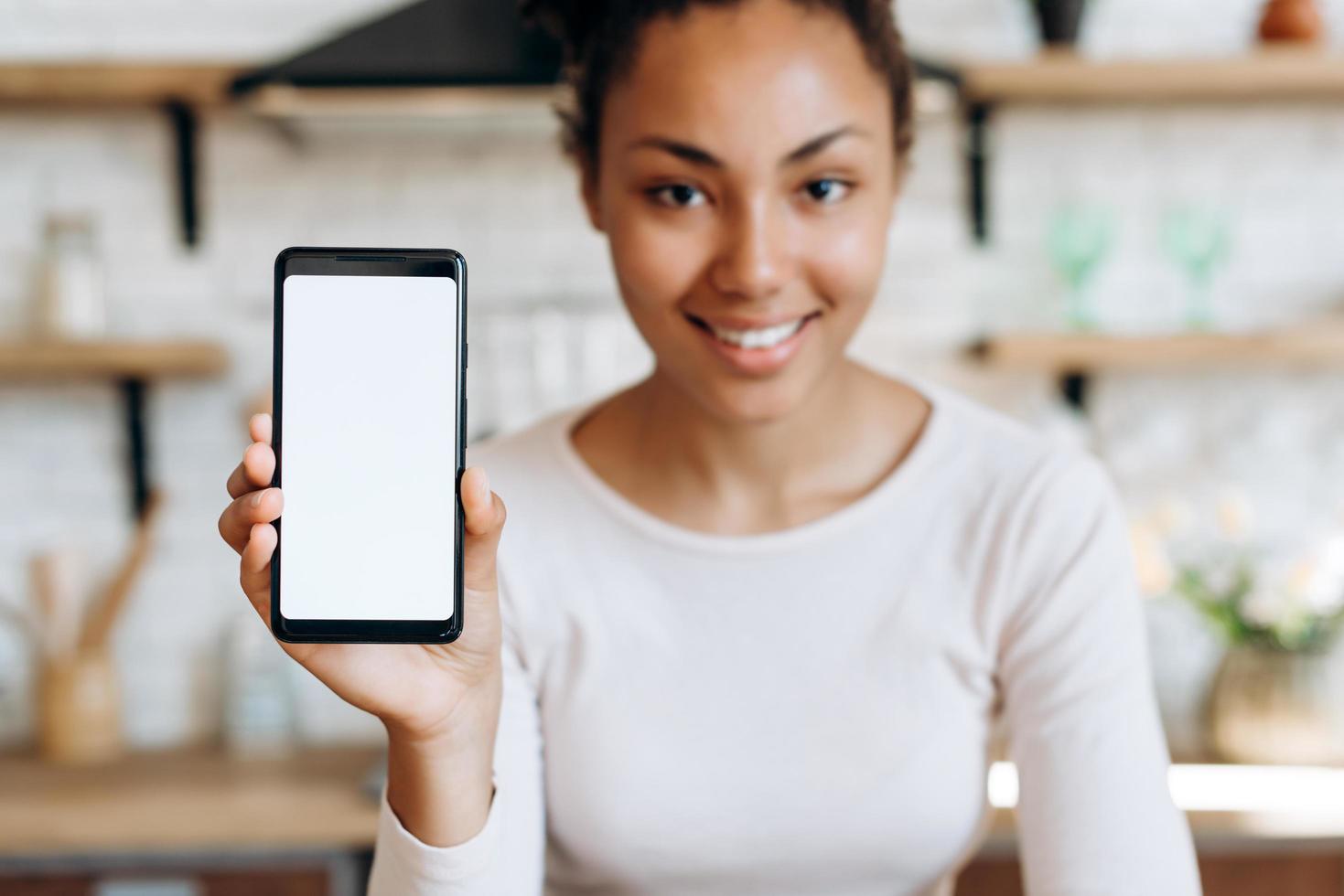 sonriente, hermosa niña sentada en la cocina, sosteniendo un teléfono en sus manos con espacio de copia foto