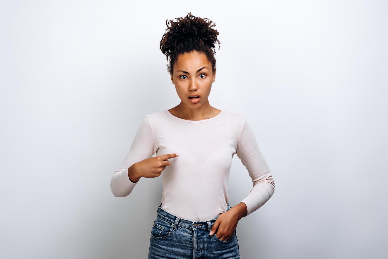 Portrait of indignant girl with chestnut hair startled, points at herself with for finger, opens mouth in surprisement, has dissatisfied expression, wears casual clothes photo