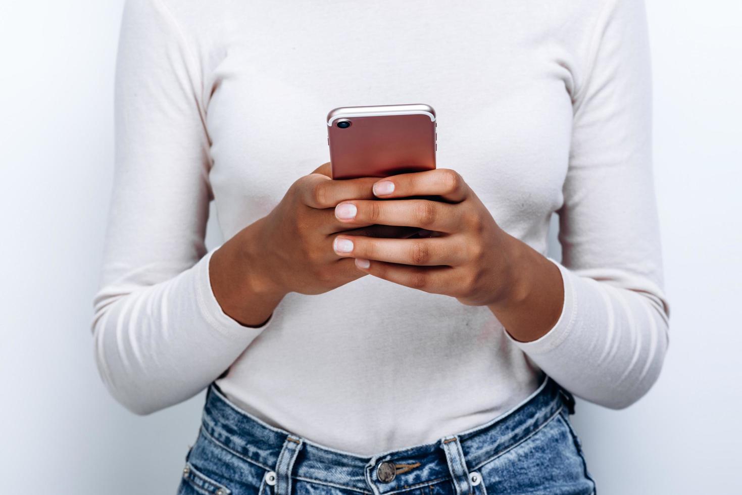 Close-up view of beautiful, tender, girlish hands holding a phone on a white wall background photo