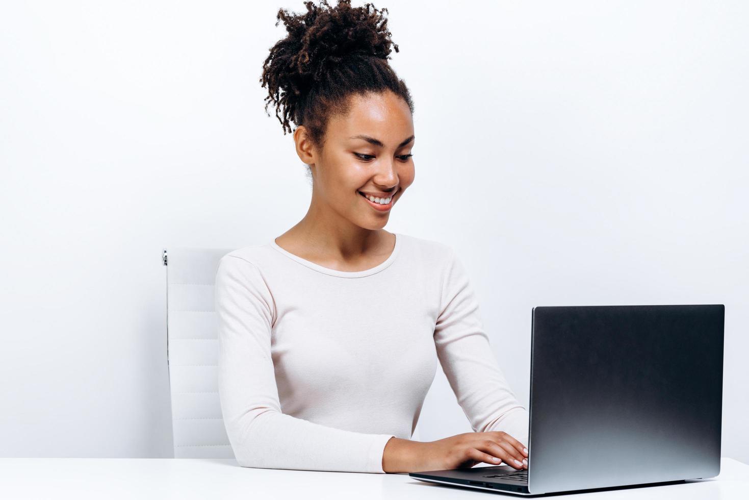 Happy young woman sitting at the table and using laptop on a white background photo