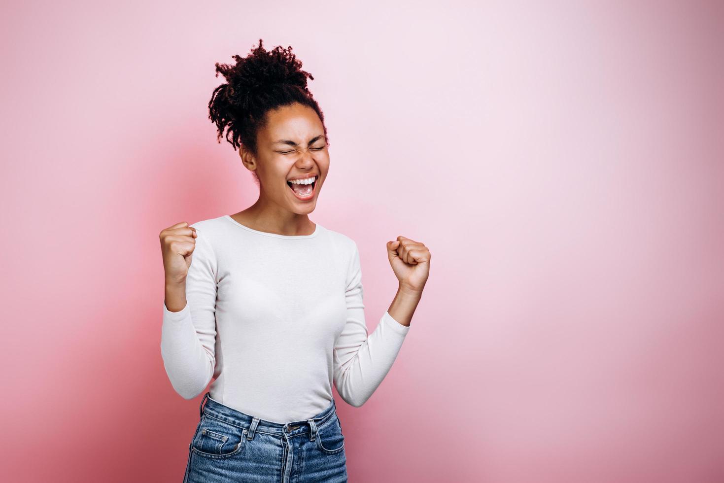 Happy young girl make winner gesture posing isolated over pink background photo
