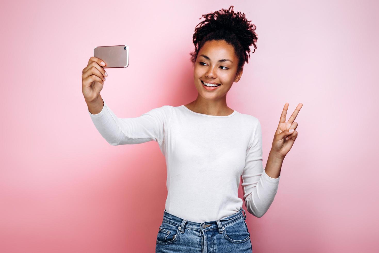 Chica atractiva sobre un fondo de una pared rosa hace un selfie foto